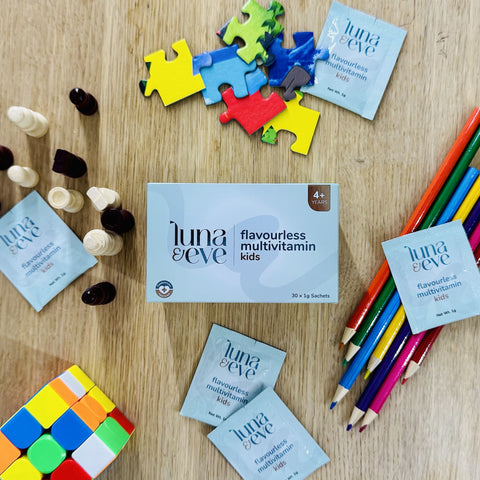 Luna & Eve multivitamin packages on a wooden surface with toys and stationery items.