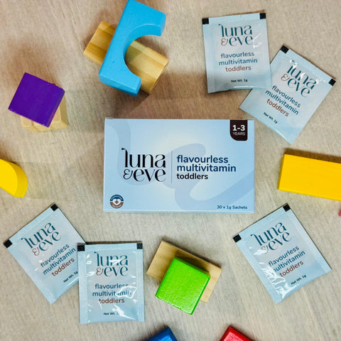 Luna & Eve flavourless toddler multivitamin powder packaging surrounded by colorful building blocks on a wooden surface.