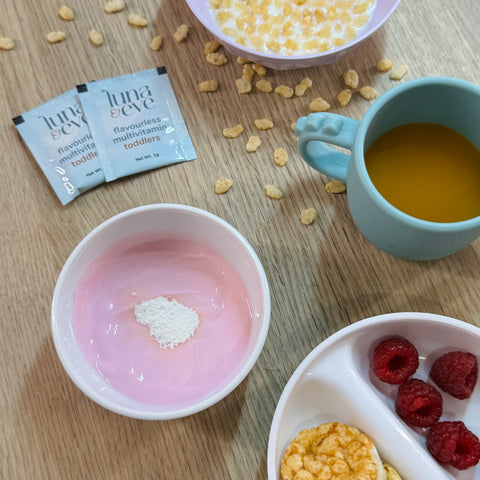 Table with various food items including a bowl of strawberry yogurt, a packet of Luna & Eve flavourless multivitamin powder, and a cup with a snack.