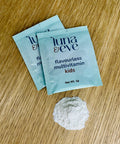 Two packets of Luna & Eve flavourless multivitamin kids on a wooden surface with powder within one sachet beside them.