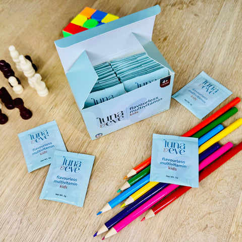 Luna & Eve multivitamin packets on a wooden surface with colorful pencils.